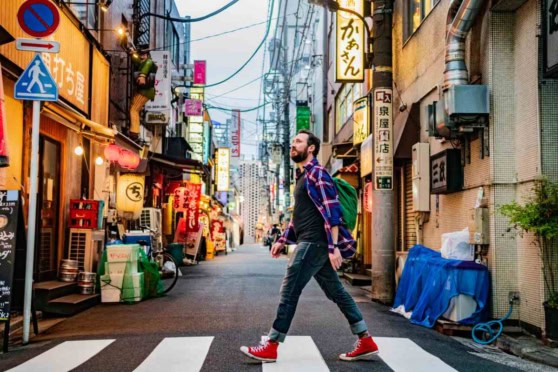 A confident man with a backpack walks through an illuminated urban street scene in Japan, showcasing international travel and city exploration.