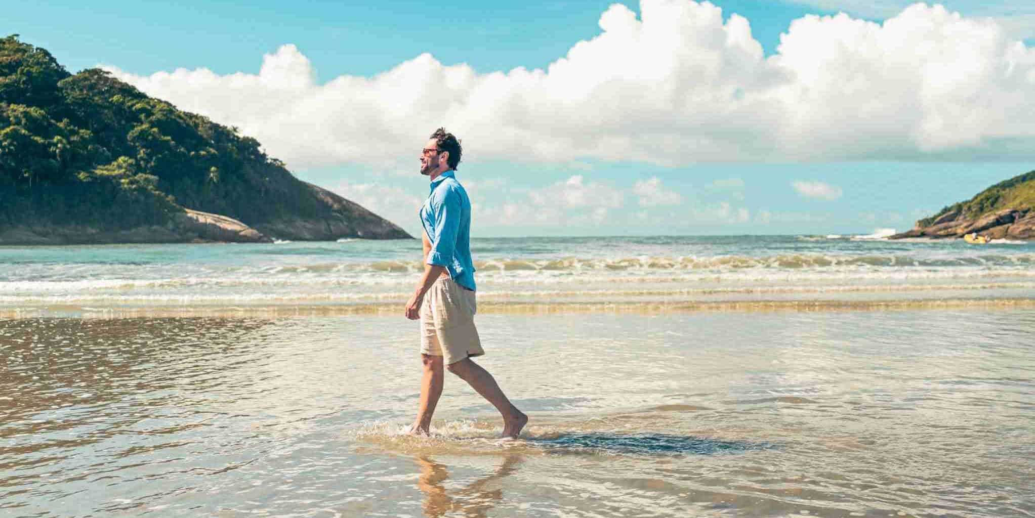 Image of a professional man enjoying a beach walk, representing travel and leisure, under a clear sky with scenic coastal cliffs, emphasizing international travel and insurance coverage.