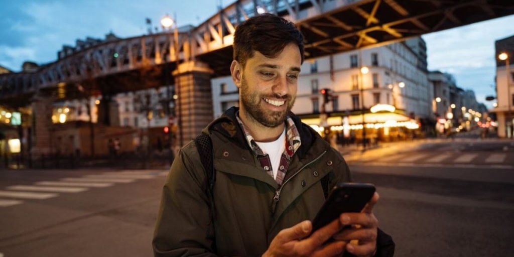 A cheerful man using a smartphone outdoors in a city, emphasizing international travel and expat insurance services offered by International Citizens Insurance.