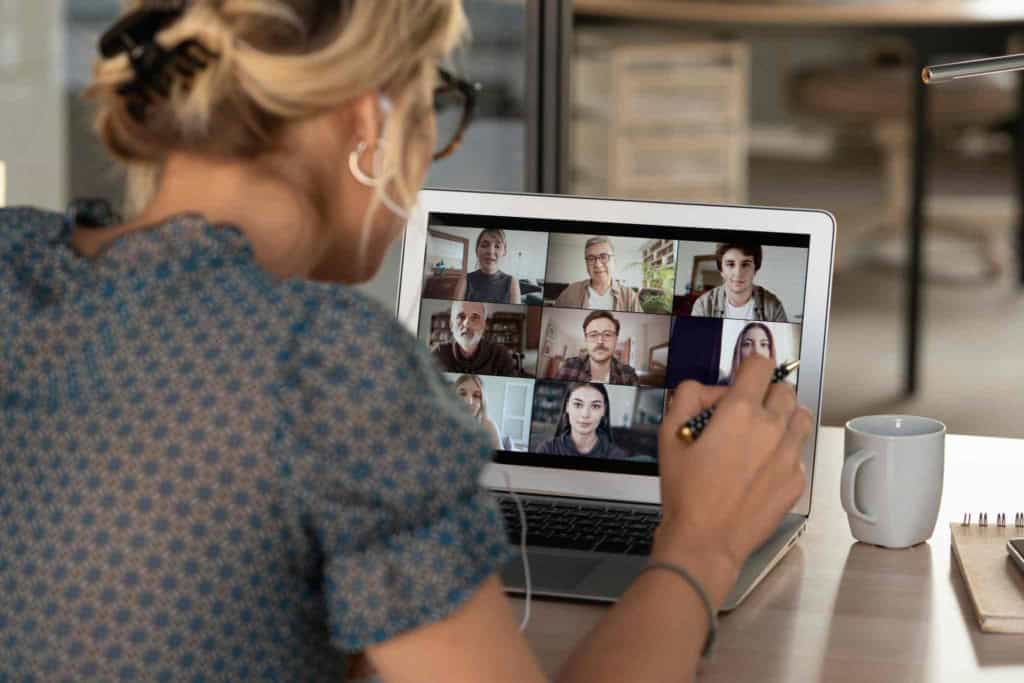 Accessible image of a woman participating in a virtual meeting with multiple colleagues via laptop, emphasizing remote communication.