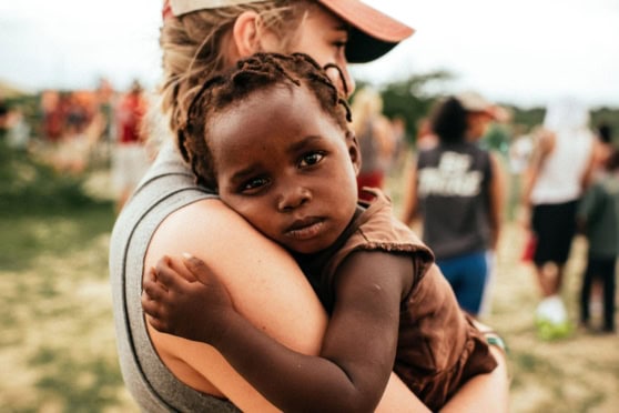 A caring woman holds a young girl with a serious expression in a humanitarian aid setting, emphasizing the importance of international health coverage for vulnerable populations.