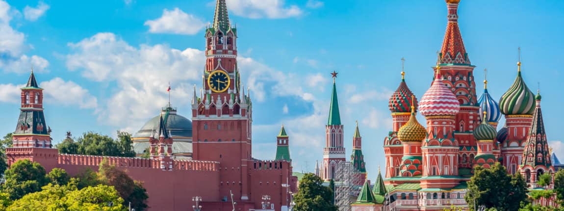 Pink and green Spasskaya Tower and colorful onion-domed St. Basil's Cathedral in Moscow, Russia, under a bright blue sky with clouds.