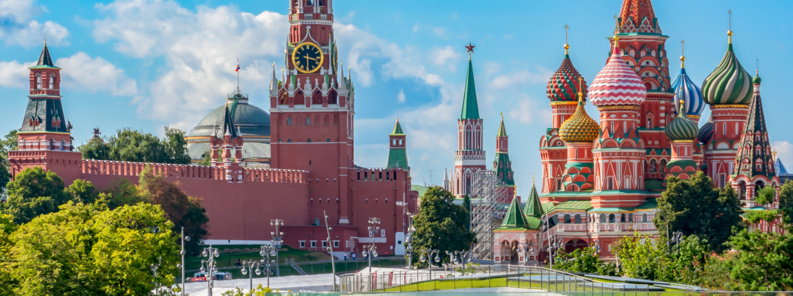 Pink and green Spasskaya Tower and colorful onion-domed St. Basil's Cathedral in Moscow, Russia, under a bright blue sky with clouds.