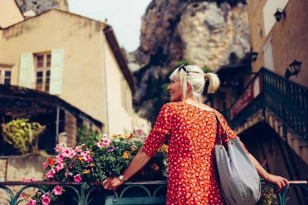 happy woman a enjoying a peaceful day in a picturesque village with traditional architecture, flowers, and rocky hills in the background, having read our top 10 travel safety tips for women