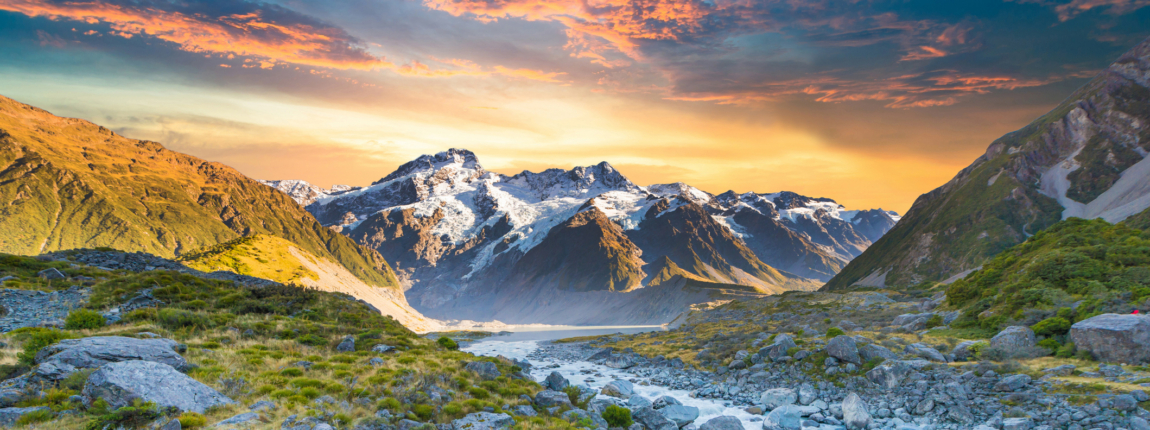 Vivid mountain landscape at sunset with snow-capped peaks, lush green valley, and flowing river, representing nature, outdoor adventure, and environmental conservation at New Zealand's scenic destinations.