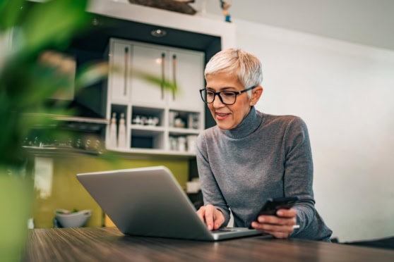 A woman using a laptop and smartphone, exploring international health insurance options with International Citizens Insurance for global coverage and peace of mind.