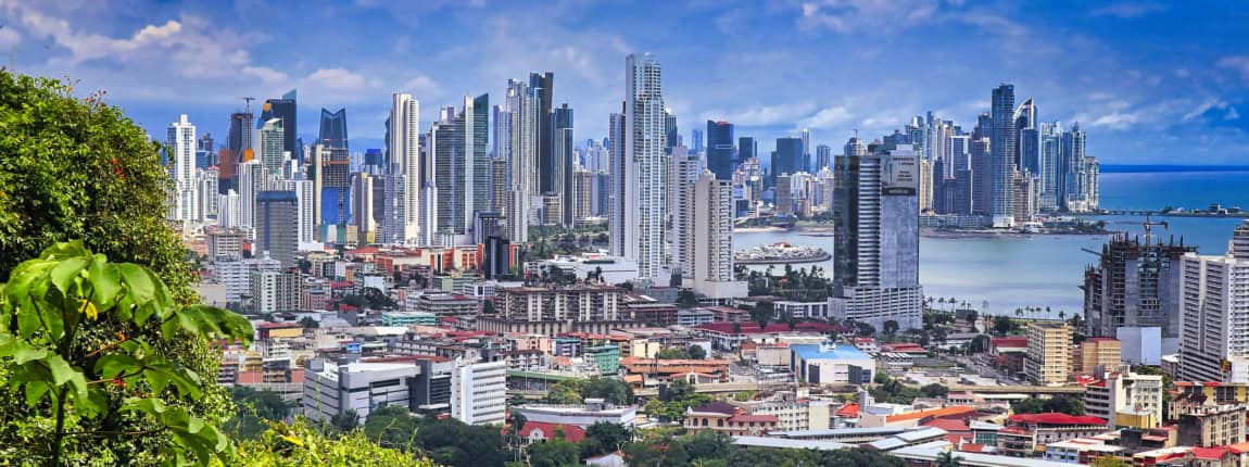 Modern skyline of Panama City with tall skyscrapers, lush greenery in the foreground, under a partly cloudy sky, highlighting urban development and nature integration.