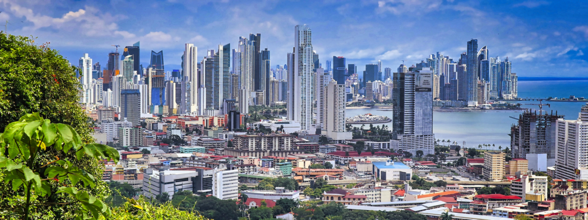 Modern skyline of Panama City with tall skyscrapers, lush greenery in the foreground, under a partly cloudy sky, highlighting urban development and nature integration.