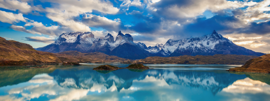 Lush mountain landscape with snow-capped peaks, reflecting on a calm turquoise lake under a dramatic sky in Torres del Paine National Park, Chile. A breathtaking view of Patagonia's natural beauty and wilderness.