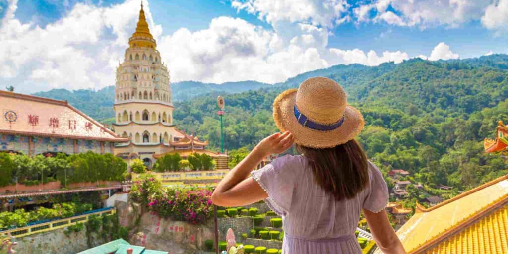 A woman wearing a straw hat overlooks a beautiful Thai temple and lush green mountains, highlighting the importance of international health insurance and travel coverage for global citizens visiting Thailand as well as understanding visa types for Thailand