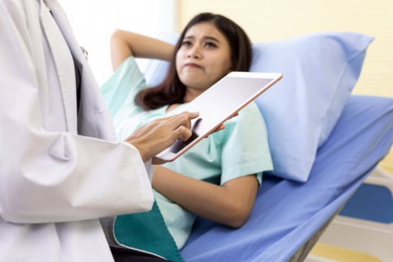 A female patient consulting with a doctor using a tablet in a hospital setting to discuss insurance coverage options and medical care details.