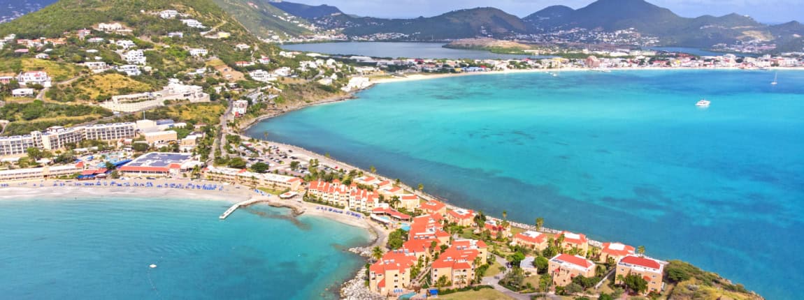 Aerial view of a tropical island with turquoise waters, sandy beaches, lush green hills, and coastal resort condos during daytime, showcasing scenic Caribbean tourism and conference destination.