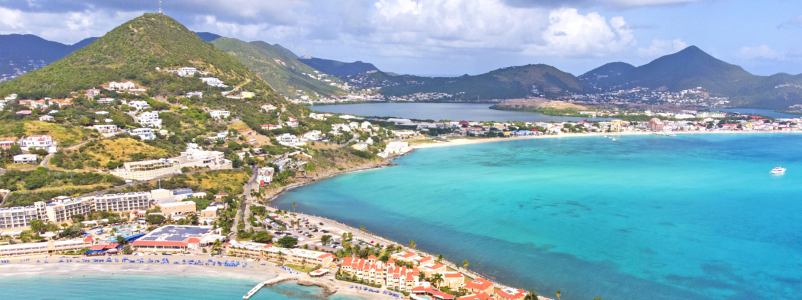 Aerial view of a tropical island with turquoise waters, sandy beaches, lush green hills, and coastal resort condos during daytime, showcasing scenic Caribbean tourism and conference destination.