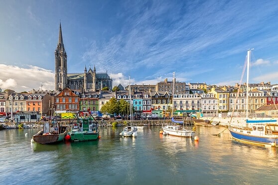 Harbor scene with sailboats, colorful houses, and a church tower in the background, emphasizing the picturesque setting for international residents and travelers.
