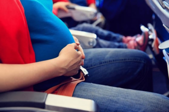 Pregnant woman on airplane, holding her belly, experiencing discomfort or travel-related health concerns.