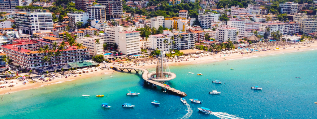 Aerial view of Puerto Vallarta’s beachfront, high-rise buildings, turquoise waters, and boats.