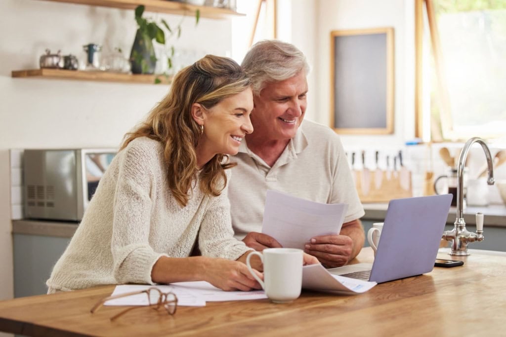 An elderly couple happily reviewing insurance documents in a cozy kitchen with a laptop, symbolizing global health coverage for expatriates and international citizens.