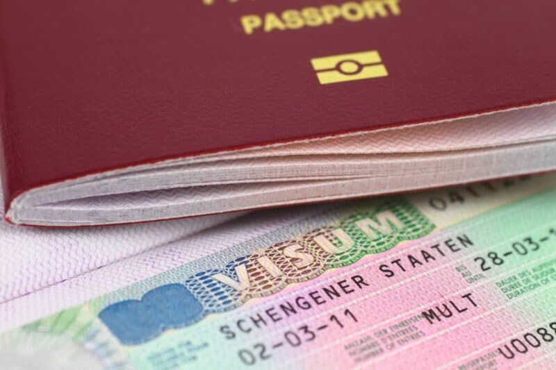 Compact passport with a Schengen visa and travel stamps, placed atop a multicolored travel document, highlighting international travel essentials for global citizens.