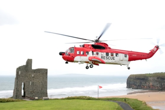 A bright red rescue helicopter hovers above a coastal landscape with an ancient castle ruin, emphasizing global emergency response for international citizens.