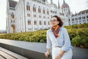 Relaxed woman in sunglasses and colorful scarf enjoying outdoors in front of the Hungarian Parliament building in Budapest, Hungary.