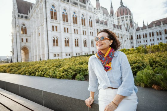 Relaxed woman in sunglasses and colorful scarf enjoying outdoors in front of the Hungarian Parliament building in Budapest, Hungary.