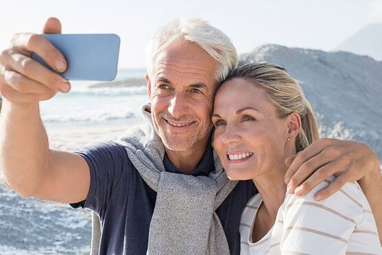 Happy senior couple taking a selfie at the beach, illustrating international health insurance options for global travelers and expats.