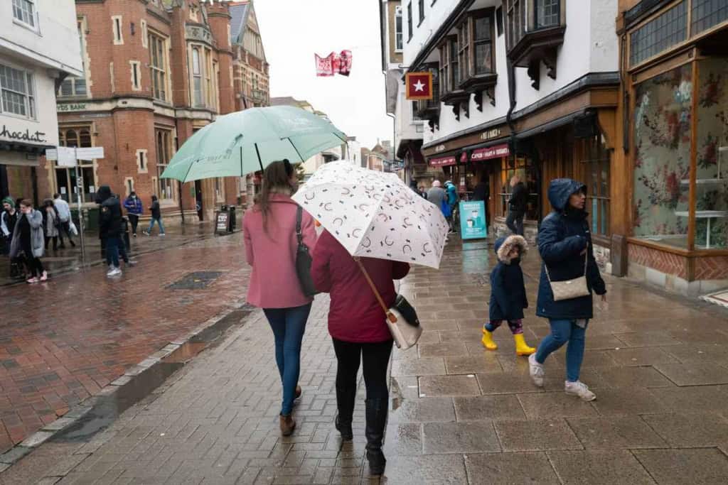 A diverse group of people with umbrellas walking on a wet city street during rainy weather, showcasing urban life and travel safety amidst rain conditions.