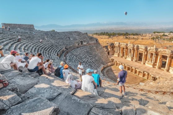 Tourists visiting an ancient Roman amphitheater, enjoying a guided tour and sightseeing at a historical site with stone seating and architecture.