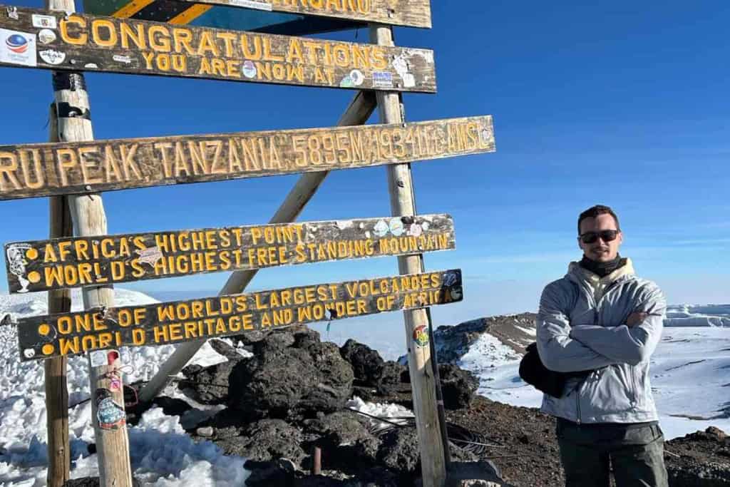 A climber standing at the summit of Mount Kilimanjaro during his adventure travel experience