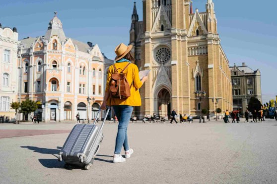 Young woman with suitcase near historic church, exploring abroad with travel insurance coverage.
