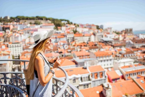 Young woman enjoying a sunny day overlooking a European cityscape, with red-tiled roofs and historic buildings.