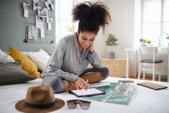 Young woman planning travel insurance options on tablet in cozy home setting with travel items.