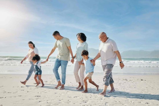 Family walking on the sandy beach, smiling and holding hands, under a bright sky, illustrating the importance of international health insurance for global travelers.