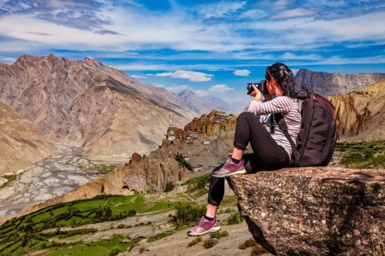A woman with a camera and backpack exploring a mountainous region with terraced fields and stunning views, emphasizing travel safety and insurance for international travelers.