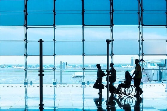 Modern airport terminal interior with travelers waiting near large glass windows overlooking tarmac.