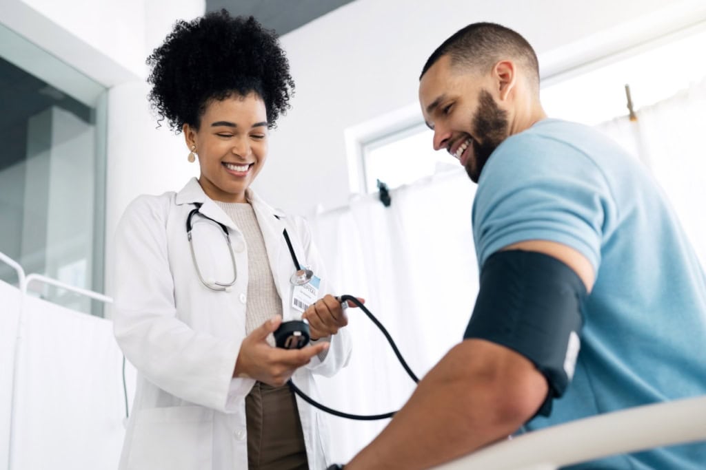 A friendly female doctor with a stethoscope assisting a smiling male patient during a medical check-up, highlighting international health insurance services.