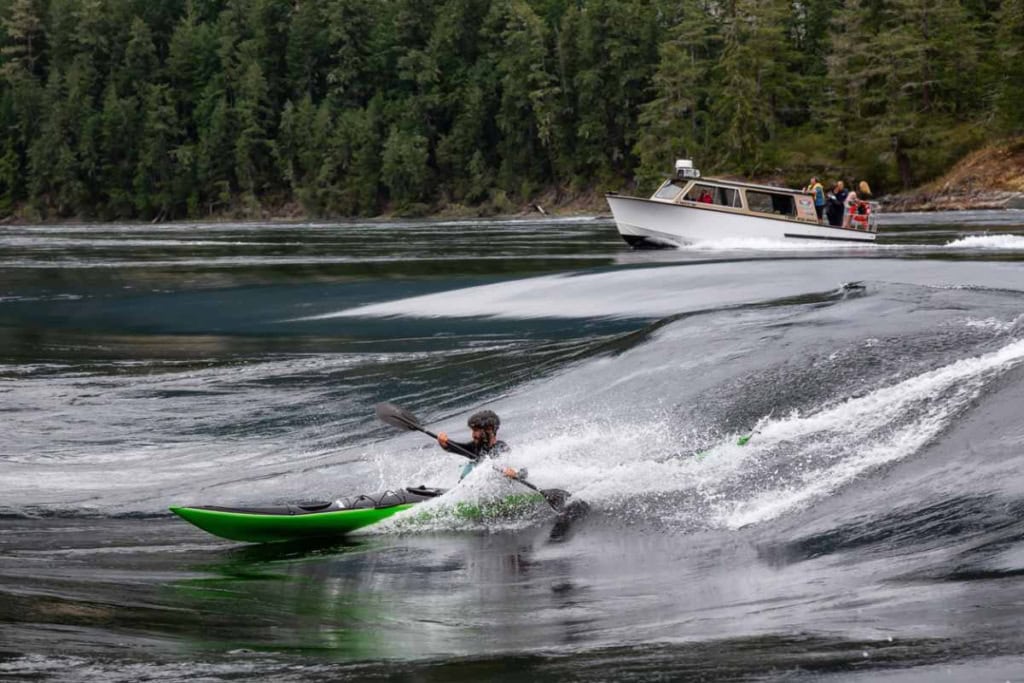 an adventurous tourist on a whitewater kayak riding a standing wave in Canada, highlighting the importance of buying travel insurance for Canada