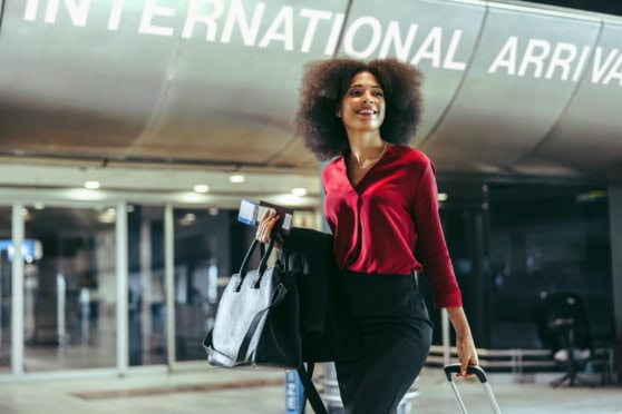 Sophisticated woman at airport arrivals with luggage, representing international insurance solutions for global citizens and travelers.