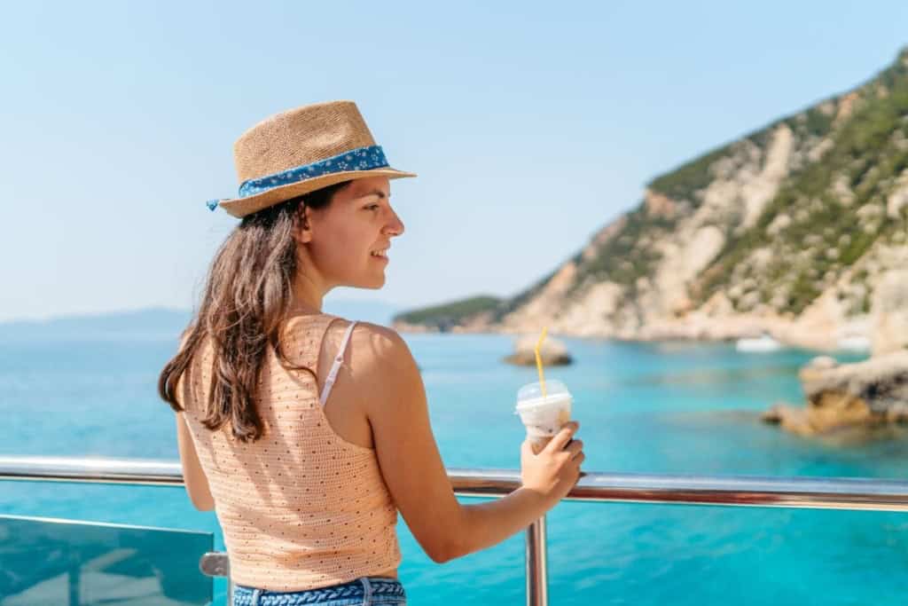 a young woman hydrating with a cold drink on the deck of a boat, having read expert cruise tips on how to stay healthy