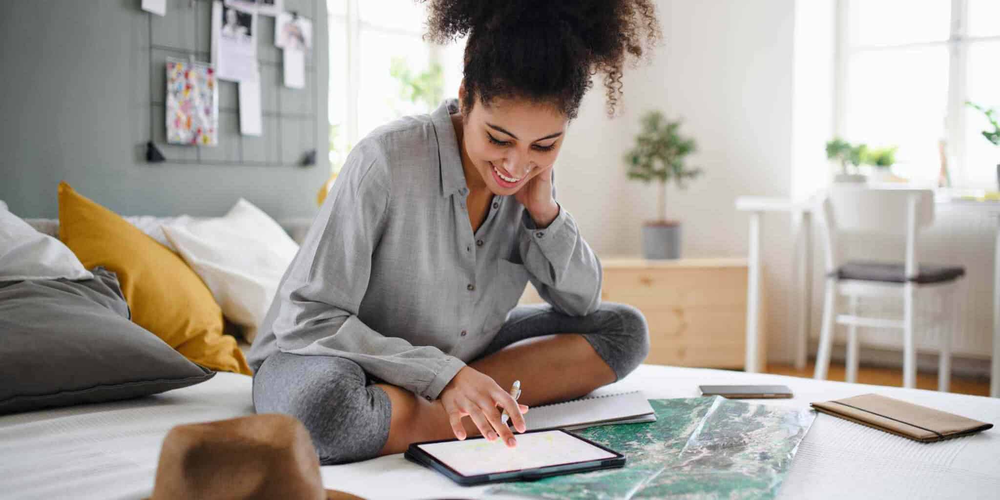 Young woman with a tablet and map indoors at home, planning a travel trip