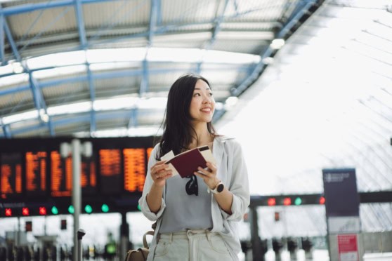 A smiling woman with a travel document at an airport terminal, representing international travel and insurance needs for global citizens and expatriates.