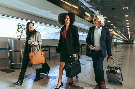 Friendly diverse professionals traveling through airport, smiling with luggage and travel documents, showcasing confidence in international insurance coverage.