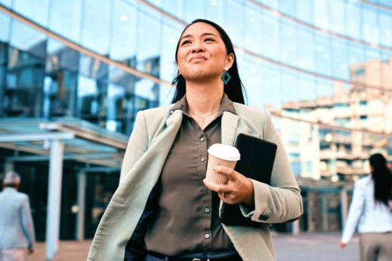 A confident woman holding a coffee cup and tablet outside a modern glass building, representing global travel and expatriate health insurance.
