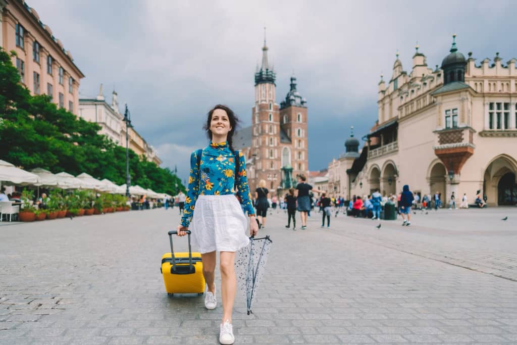 Walks through European city with suitcase and umbrella, highlighting international travel, tourism, and the importance of global health insurance plans.