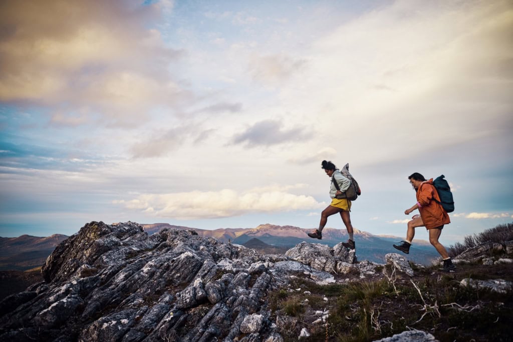 Two hikers navigating rocky mountain terrain during outdoor adventure under dynamic sky.
