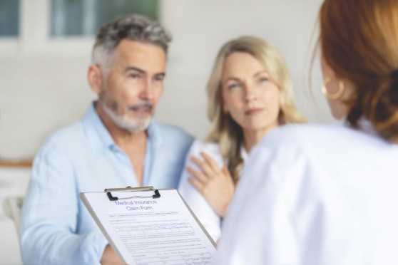 A middle-aged man and woman discuss medical insurance options with a healthcare provider, reviewing a claim form, in a professional and caring setting to emphasize global health coverage and personalized insurance plans.