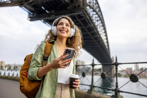 Young woman traveler enjoying cityscape view with headphones and coffee under a bridge.
