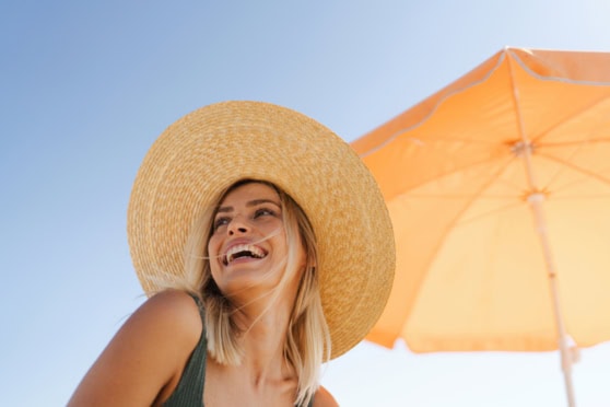 Bright image of a smiling woman with a sun hat and umbrella on a sunny day.