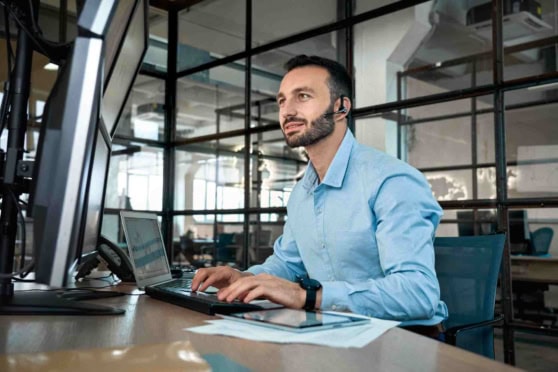 Diverse man with headset working at his desk on computer in modern office for global insurance solutions.