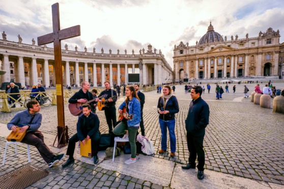 Street musicians performing in Piazza San Pietro, Rome, with historic architecture and tourists enjoying the lively atmosphere.